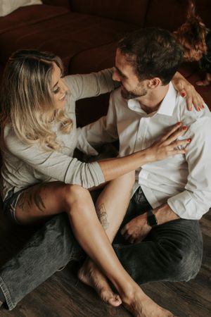 Couple sharing affectionate moments on a wooden floor in natural light.