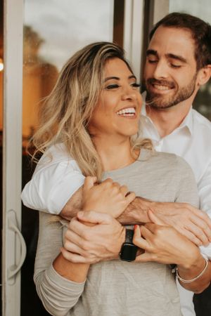 Couple laughing and embracing while wearing casual clothes indoors.