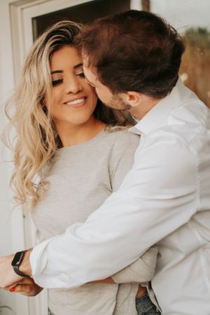 Couple sharing tender embrace against white wall in natural light.