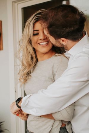 Couple sharing joyful embrace by window in warm natural lighting.