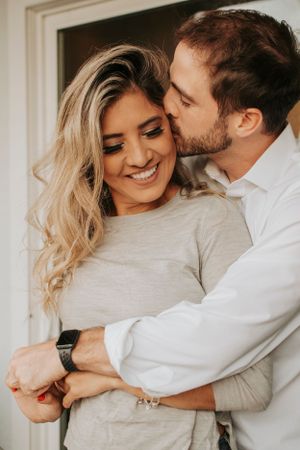 A romantic couple sharing an intimate moment as he kisses her temple while she smiles with closed eyes.