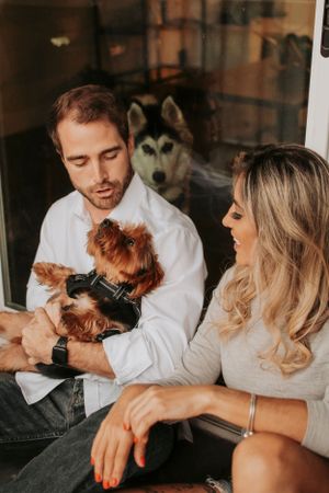 Couple sitting with their pets including a Yorkshire Terrier and Husky dog in a cozy indoor setting.