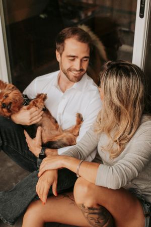 A couple playing with their small brown dog while sitting together on the floor.