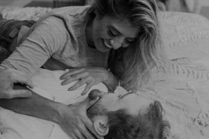 Intimate couple sharing tender moments lying on white bedding in black and white photography.