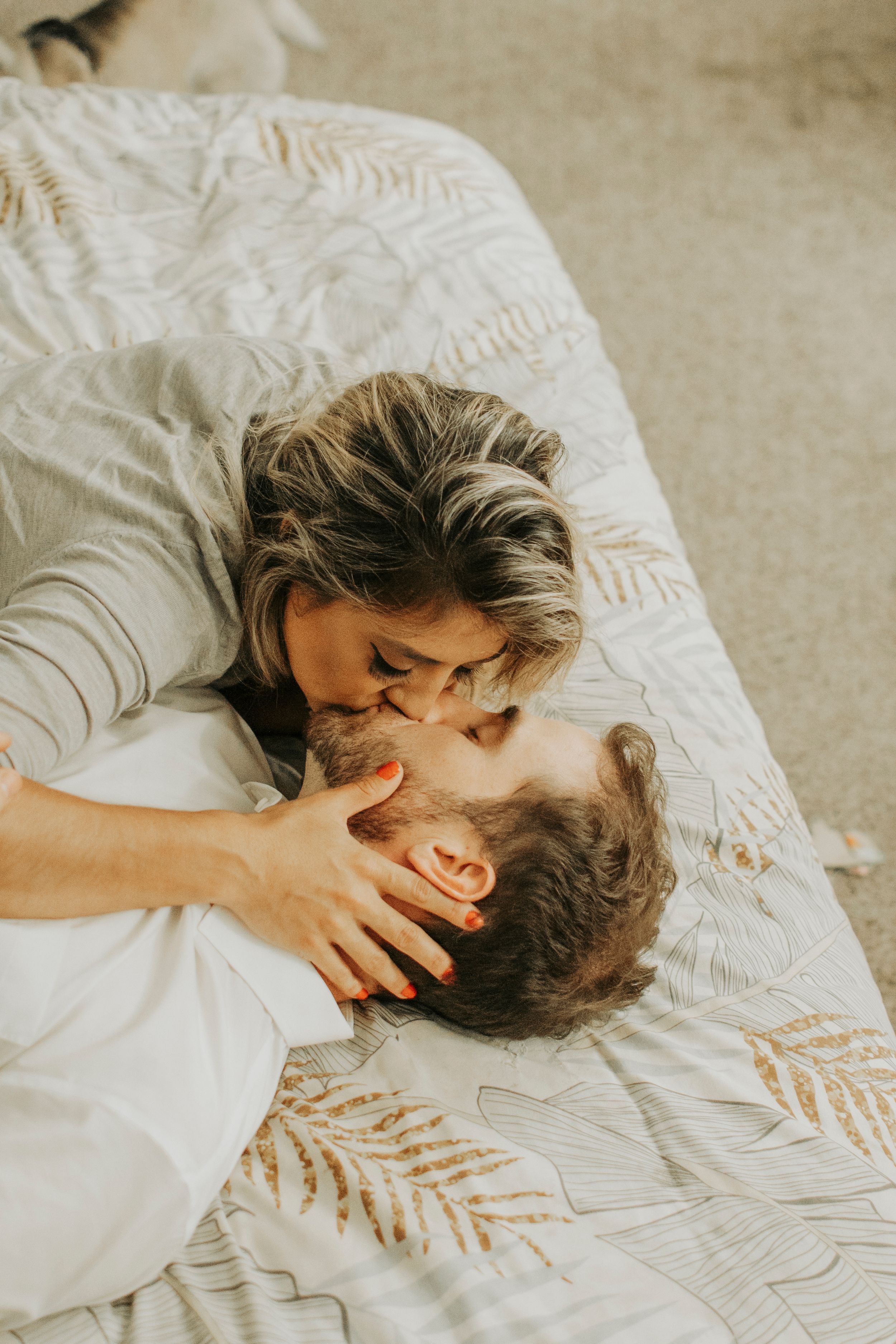 Romantic couple sharing intimate moments on textured bedding in warm tones.