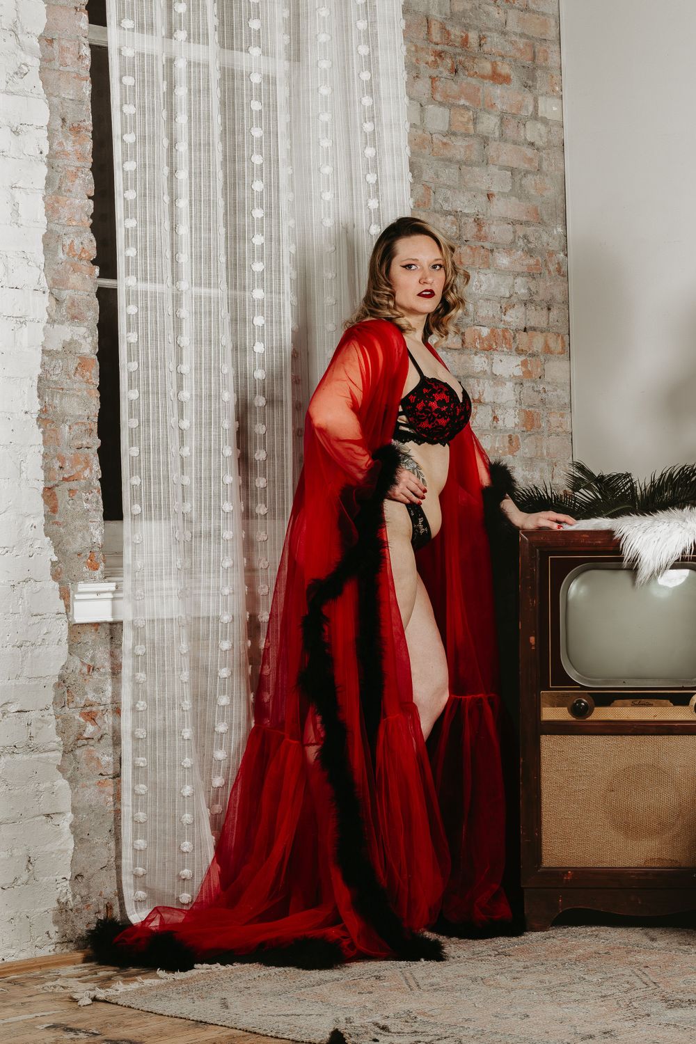 Glamour portrait featuring flowing red robe and vintage-style lingerie against industrial backdrop.