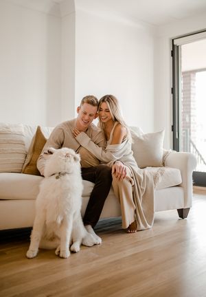 A couple relaxes on a couch with their fluffy white dog in a bright modern living room.