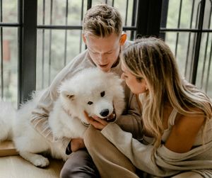An intimate moment shared between a couple and their happy white dog by a window.