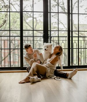A joyful couple laughs while sitting with their white Samoyed dog on hardwood floors.