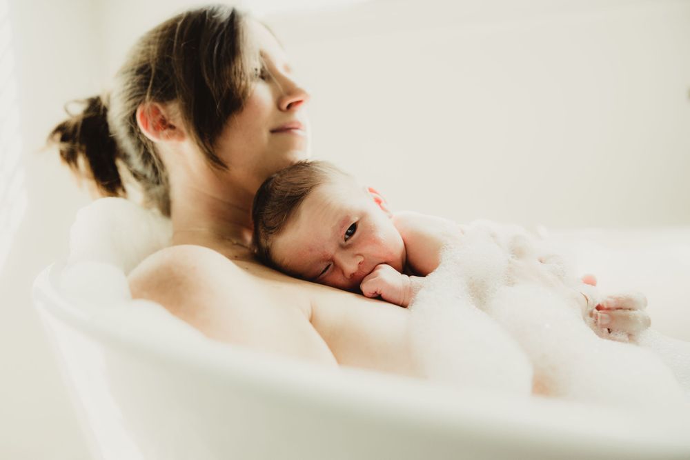 Mother holding baby on chest in bubble bath at in home newborn lifestyle photo session in Wellesley, MA