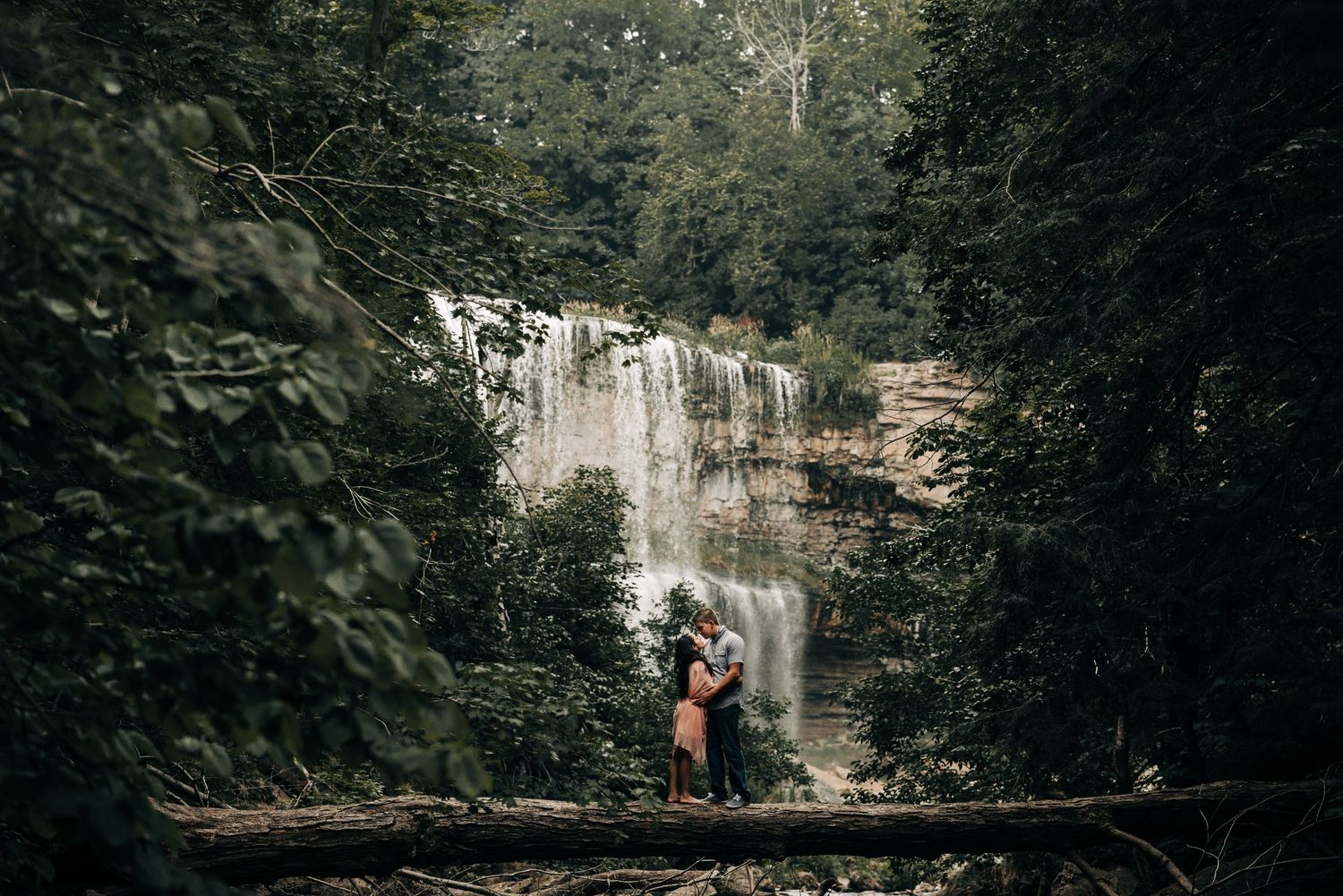 Romantic couple silhouetted against a majestic waterfall in a forest setting.