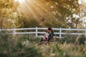 Mom and baby sitting in front of a white fence, under the sunlight