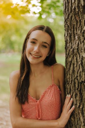 A teen girl standing up against a tree with her hand resting on it