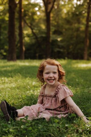 a little girl sitting in the grass, smiling happily