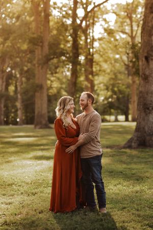 a couple standing in front of sunlit trees, facing each other