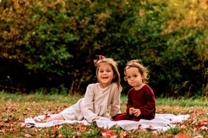 two little girls sit under fall colored trees