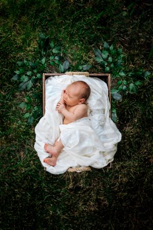 newborn baby boy wrapped in white, sitting in the grass