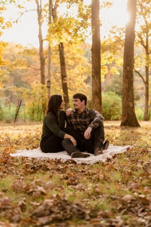 Couple sitting on a blanket looking at each other with fall leaves all around them.