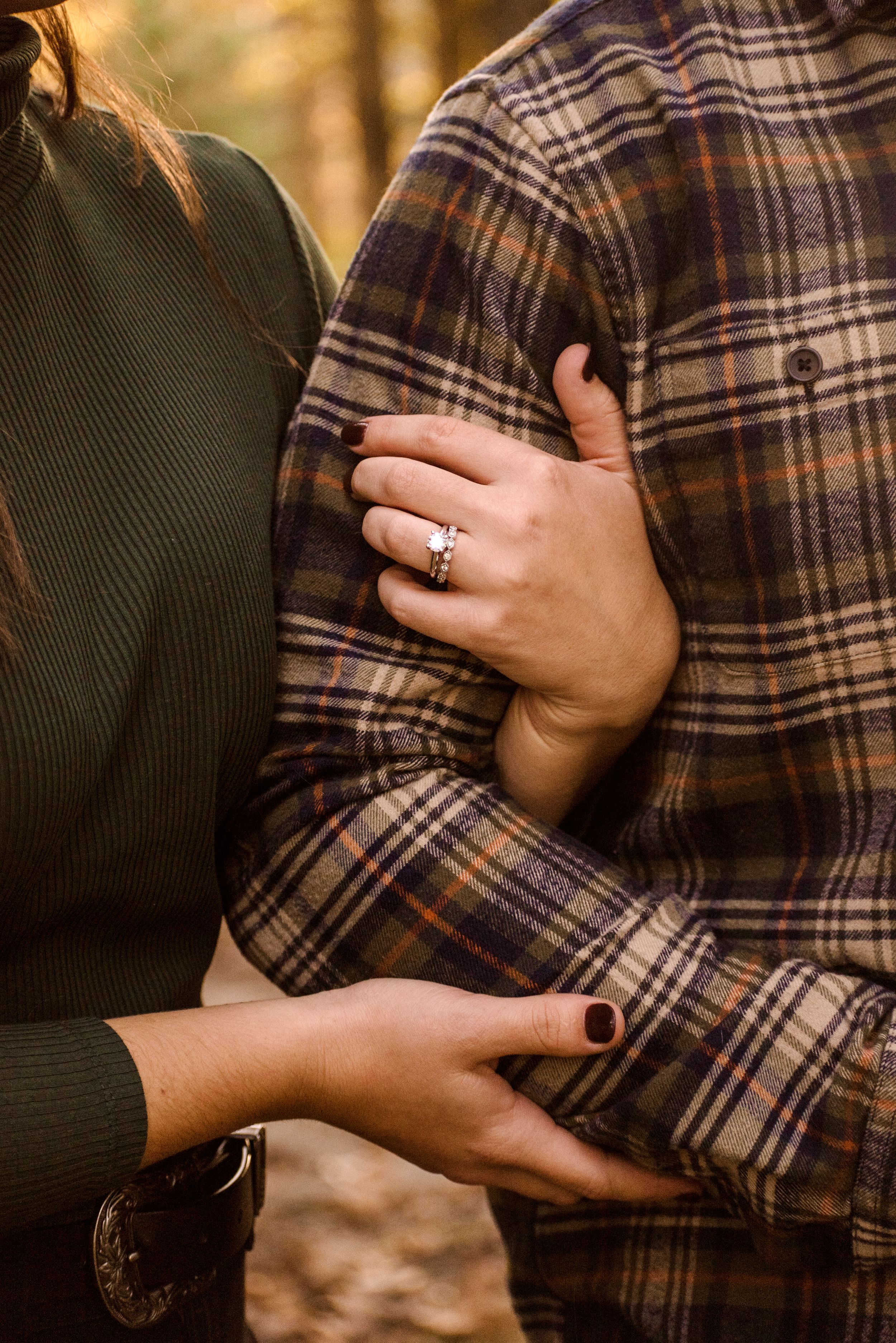Close up of womans hands wrapped around mans arm showcasing her ring.