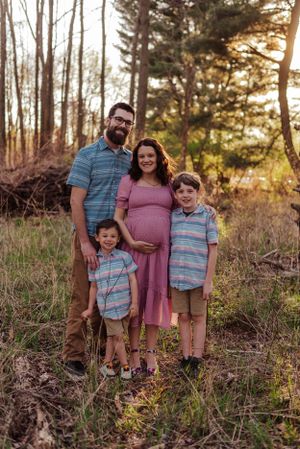 Family with 2 little boys and pregnant mom standing together with a sunset glow.