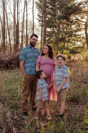 Family with 2 little boys and pregnant mom standing together with a sunset glow.
