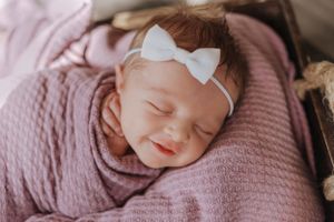 newborn girl, wrapped in pink with a white bow smiling