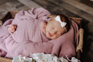 newborn girl, wrapped in pink with a white bow smiling.