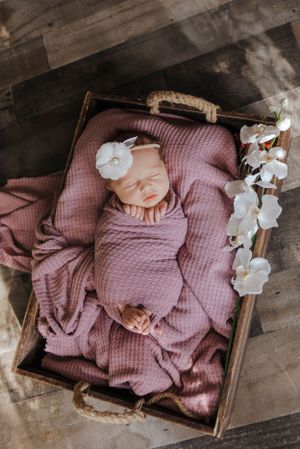 a newborn baby girl, wrapped in pink with a white flower bow