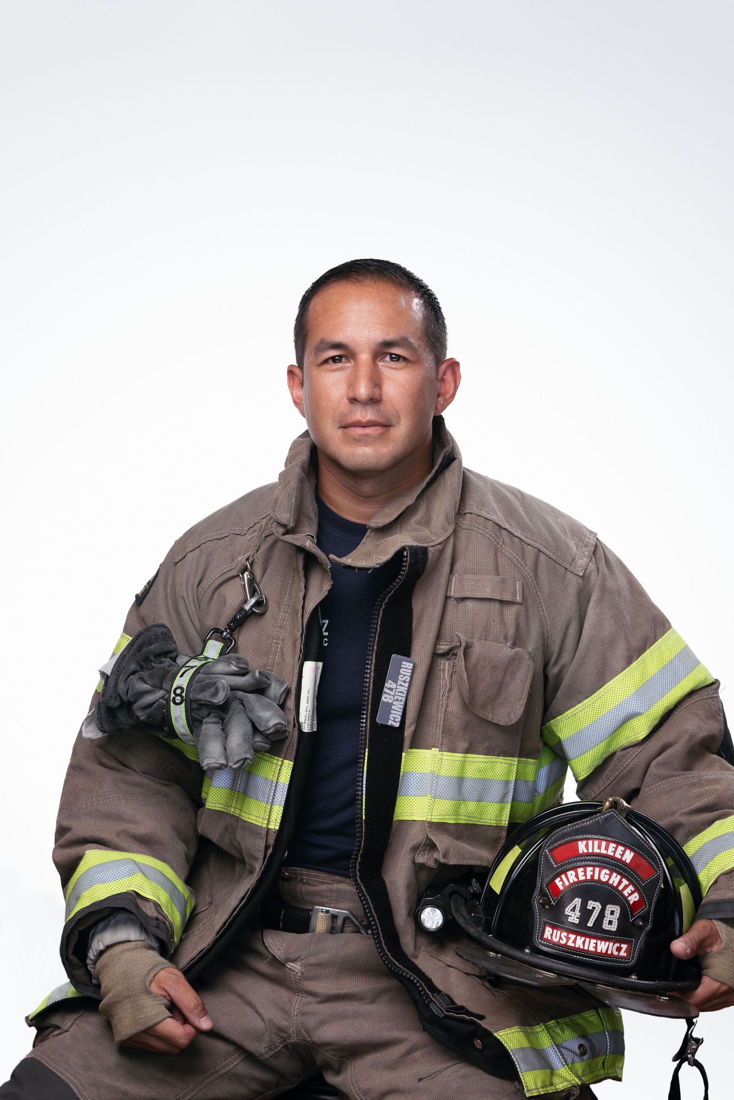 Firefighter in full gear holding helmet against white background.