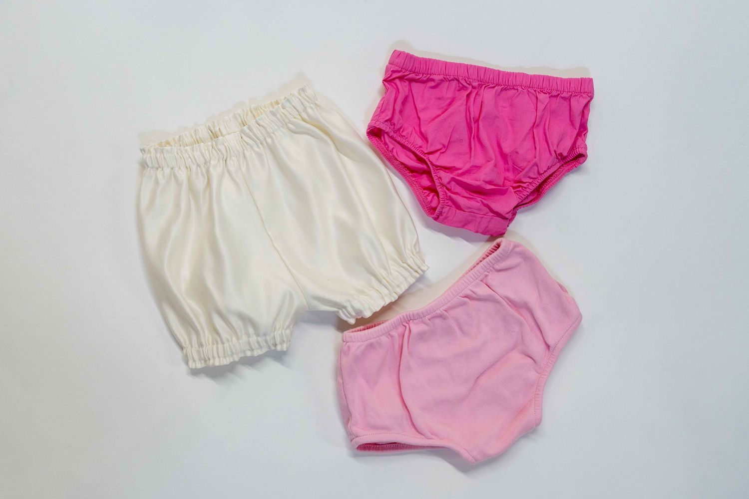 Three baby bloomers in white, pink and hot pink colors arranged on white background.