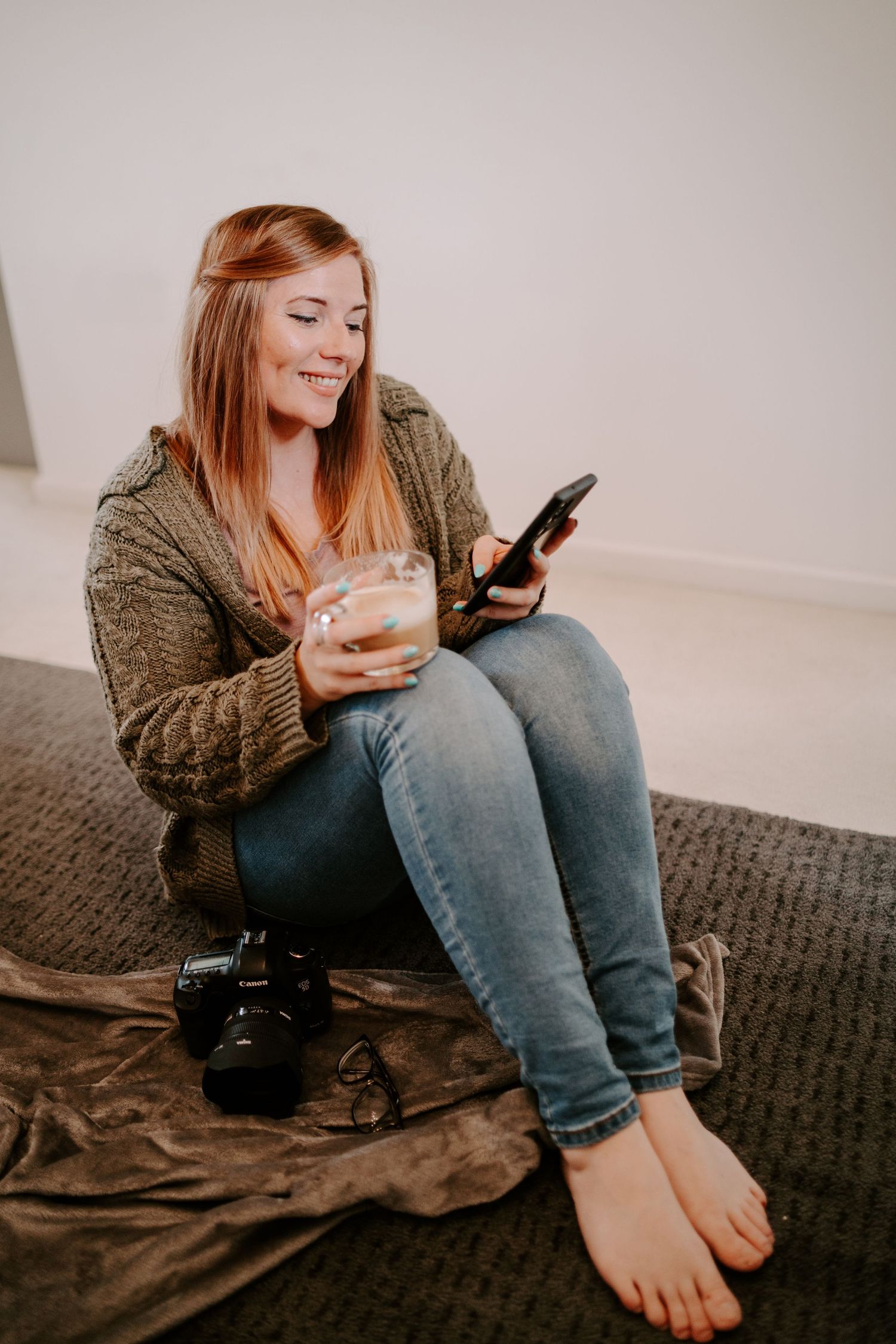 Casual indoor scene of someone in a brown sweater and jeans relaxing on a dark couch while using their phone.