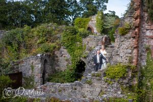 A wedding photoshoot at ancient stone ruins covered in climbing ivy and greenery.