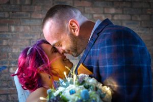 An intimate moment with colorful hair and a bridal bouquet against a brick wall background.