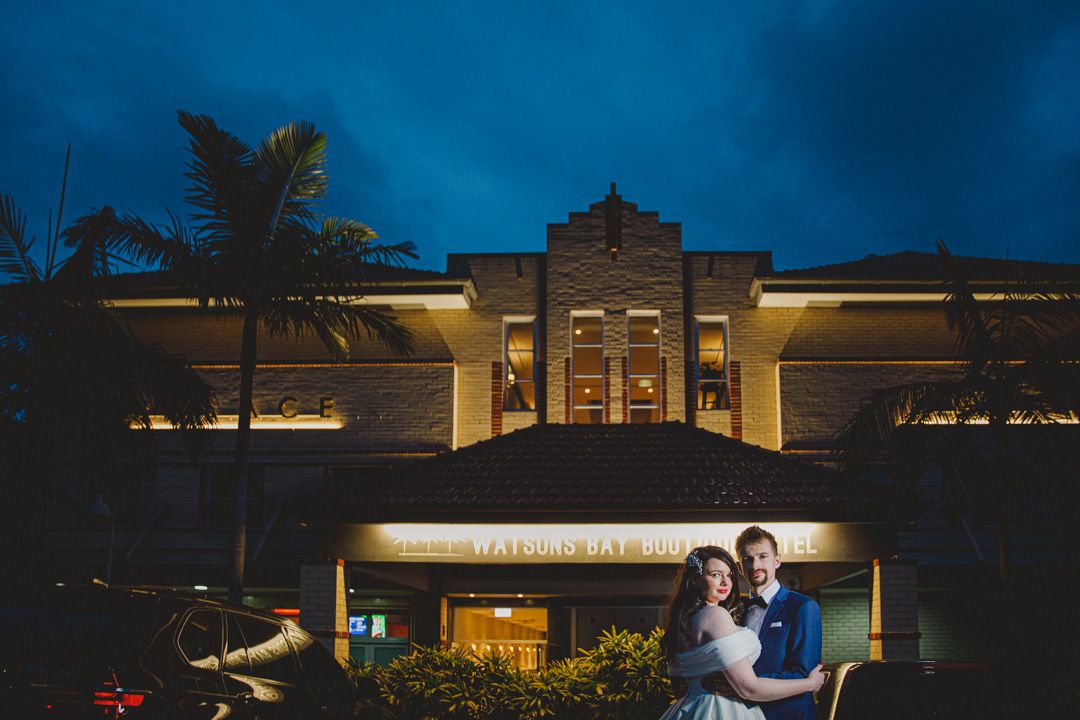 Evening wedding photos with dramatic blue sky and illuminated building backdrop.