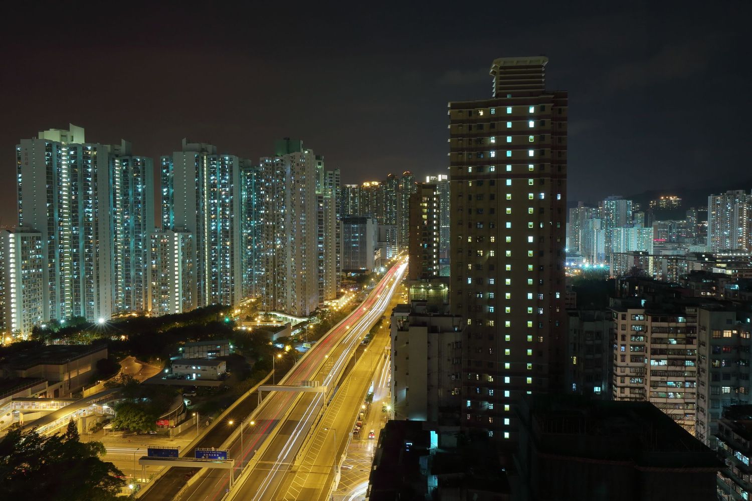 Illuminated highway and high-rise buildings in Hong Kong at night with glowing cityscape.