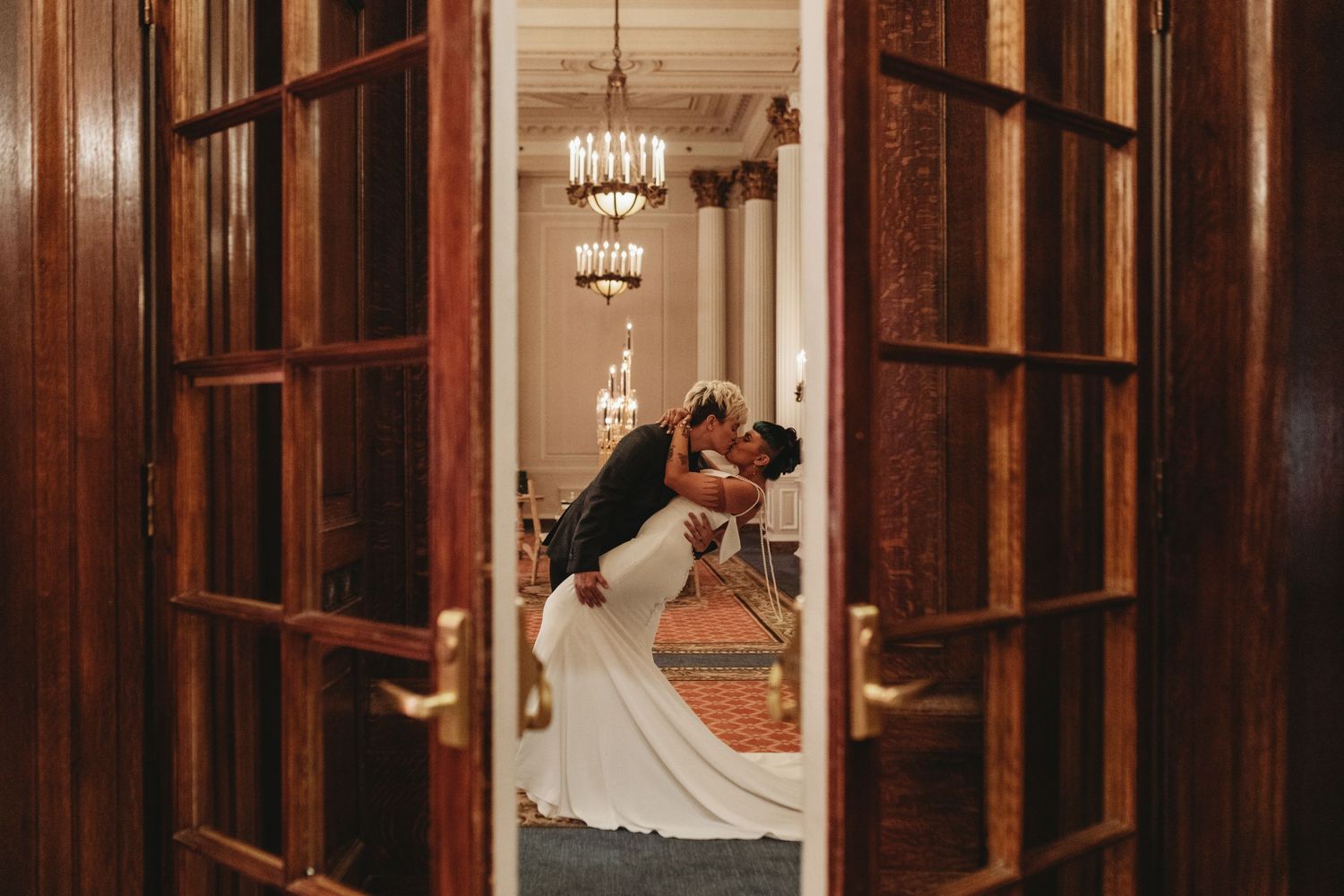 A romantic wedding moment captured through wooden doors in a warmly lit interior.