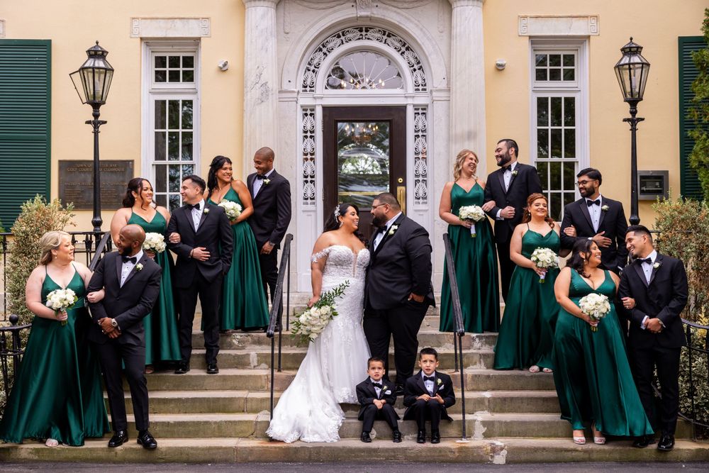 Wedding party in emerald green dresses posed on grand stone steps with couple.