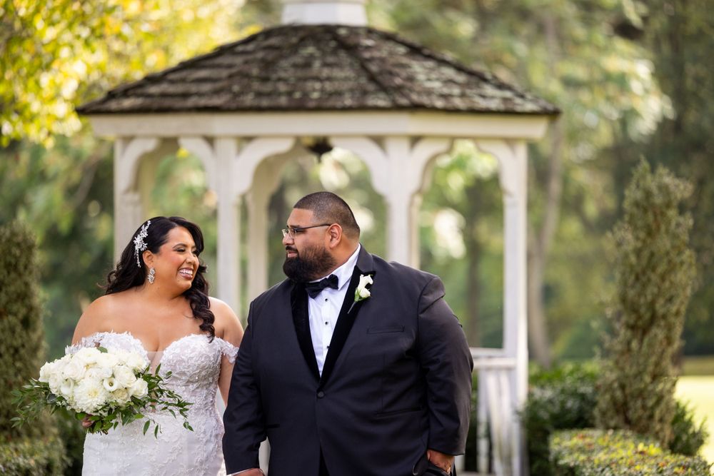 Wedding couple standing together in front of white garden gazebo.