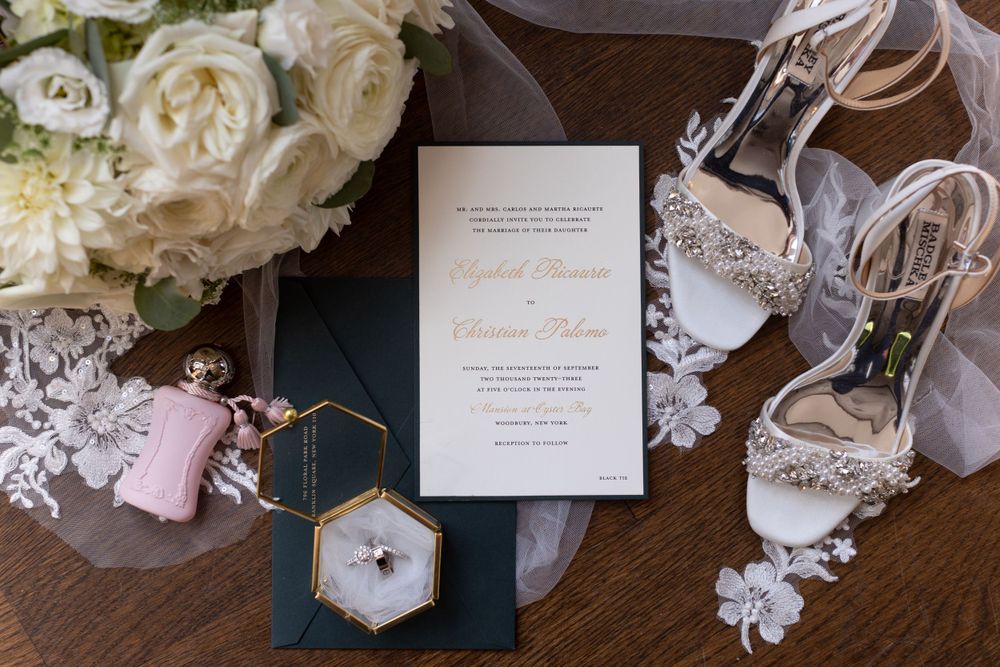 Wedding invitation displayed with bridal shoes, flowers and jewelry in an elegant flat lay composition.