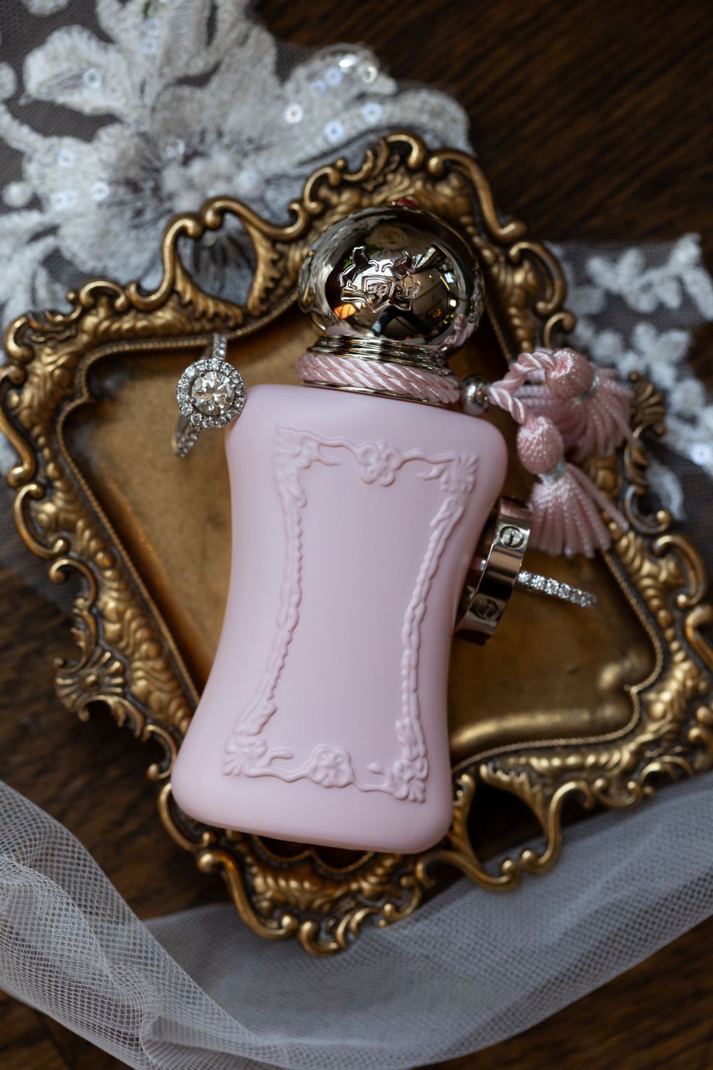 Pink perfume bottle and jewelry displayed on ornate gold vintage tray with decorative elements.