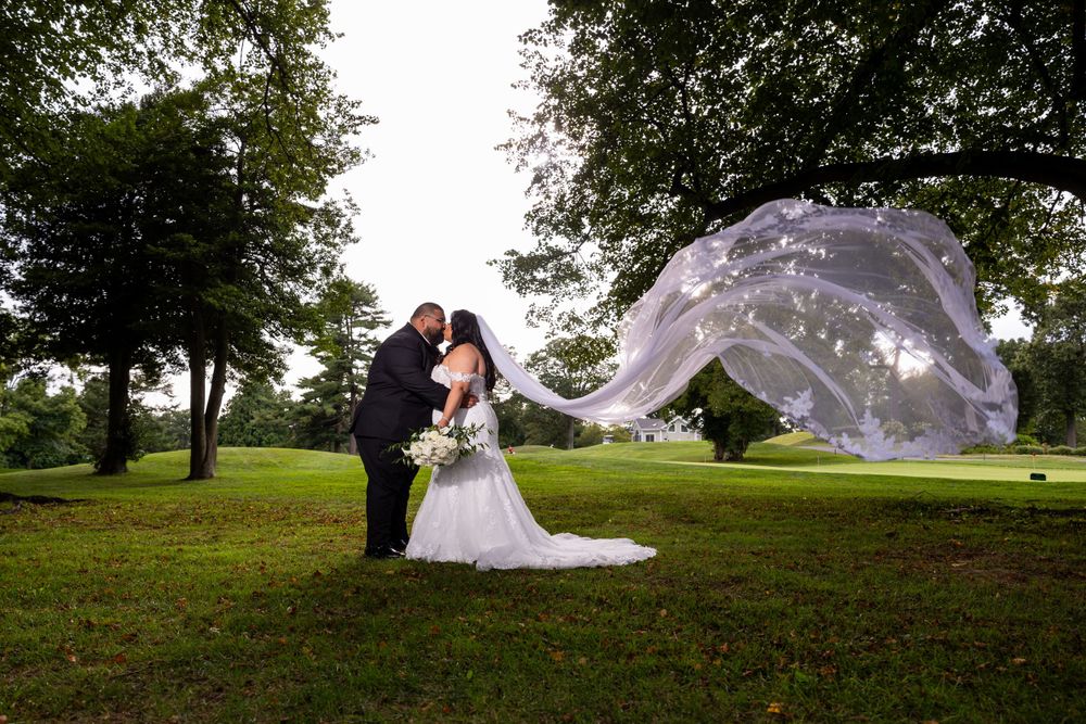 A dramatic wedding photo on a green lawn with the bride's veil floating elegantly in the breeze.