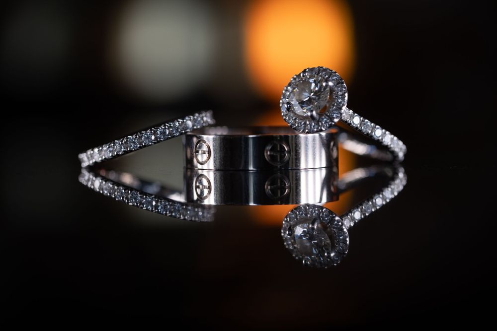 Wedding rings and bands with diamonds displayed artistically against dark background with bokeh lighting effect.