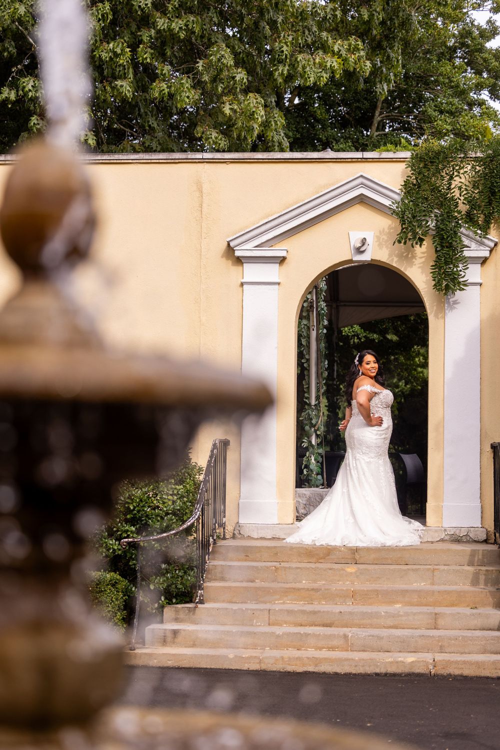 Bride in white dress standing in arched doorway of cream colored building.