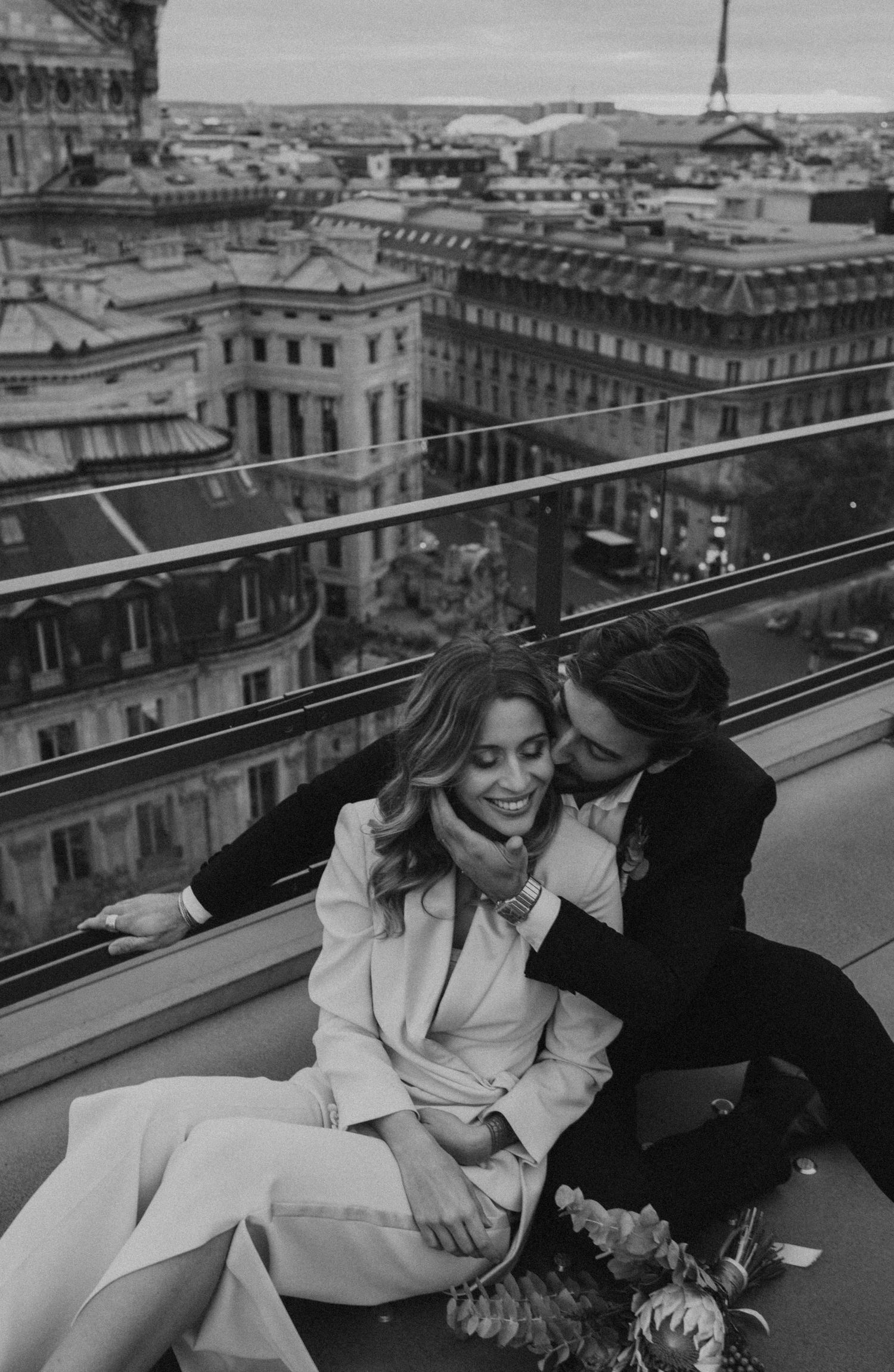 Couple shares tender moment on Parisian rooftop with cityscape views.