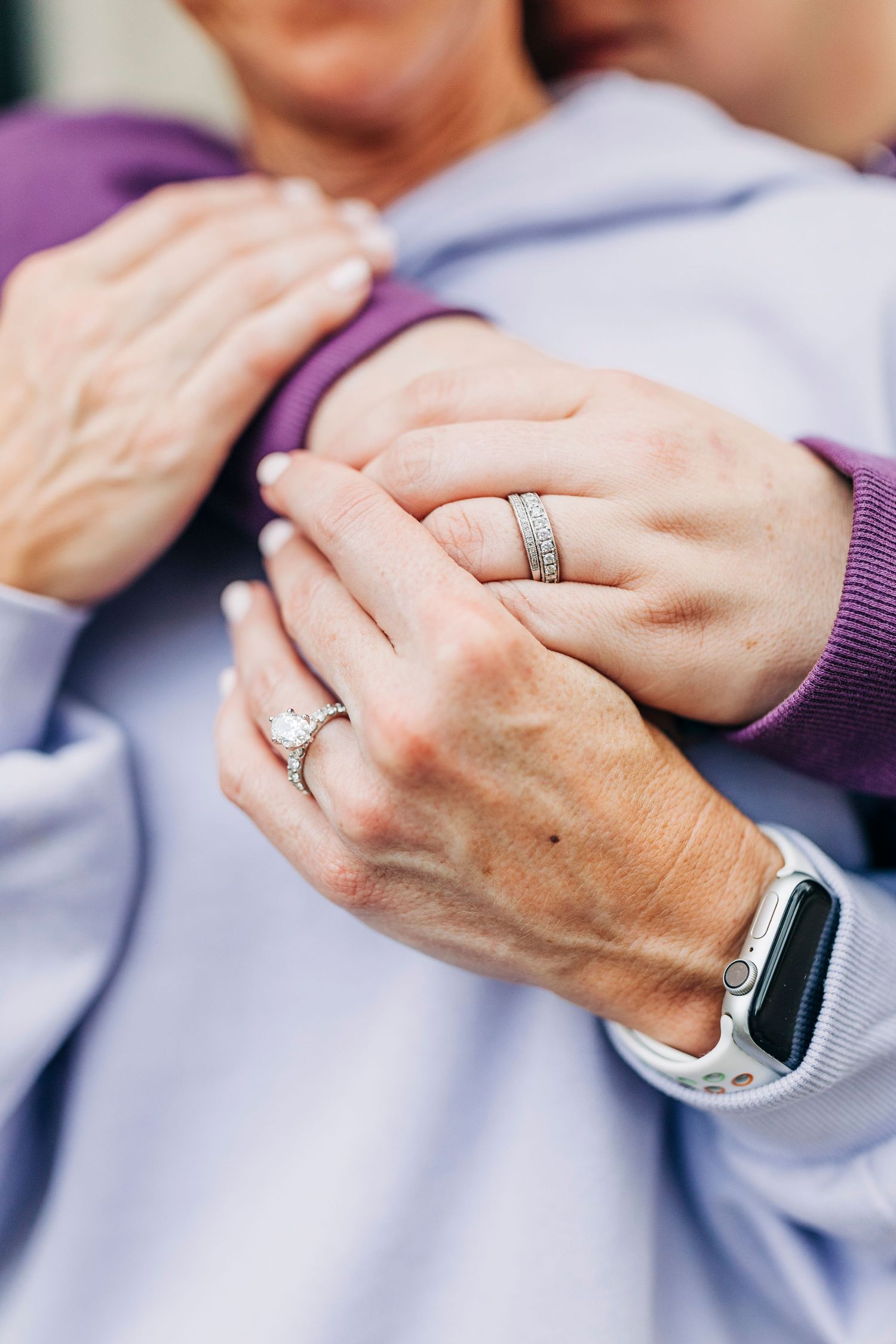 Close-up of hands showing engagement rings while embracing in casual sweaters.
