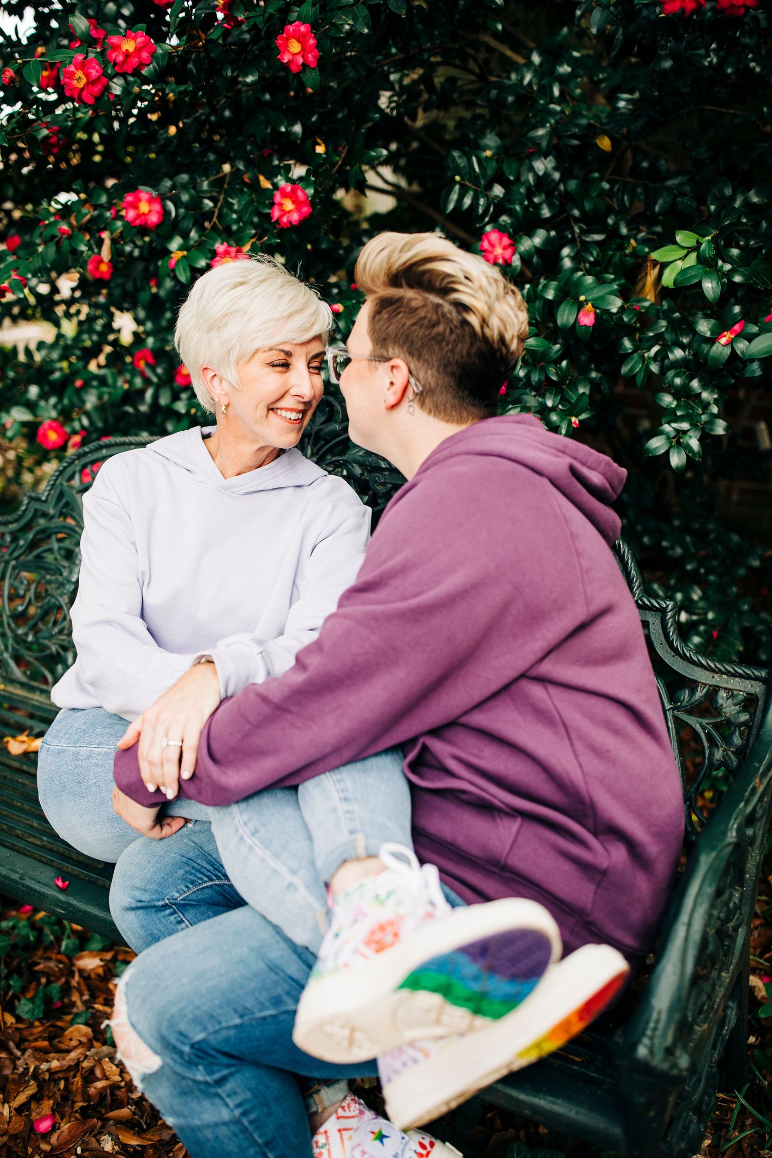 Couple sharing tender moment on bench surrounded by blooming red flowers.
