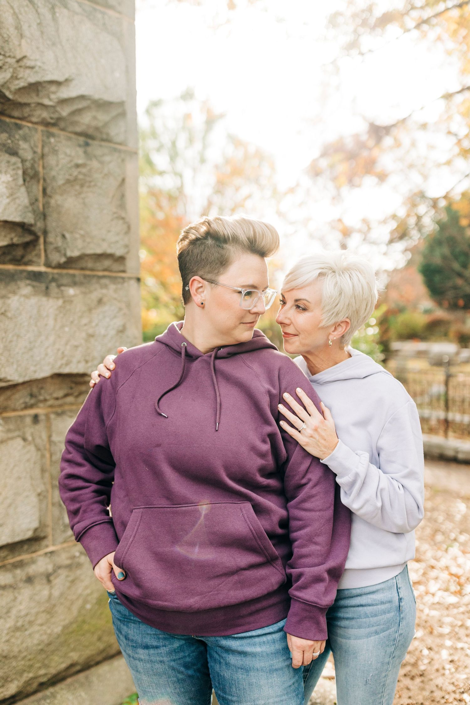 Intimate portrait of couple in casual hoodies standing against stone wall.