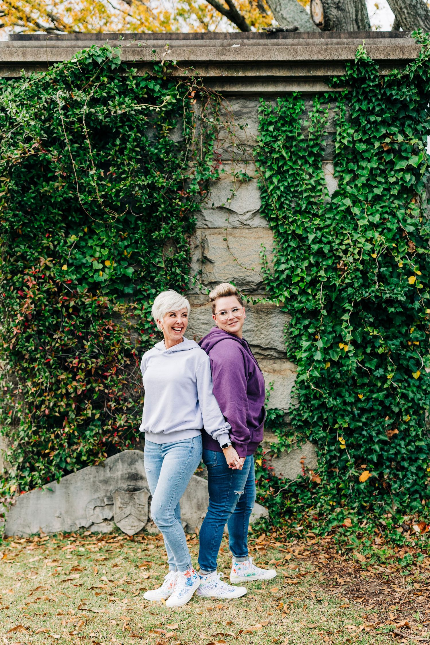 Couple posing together against an ivy-covered stone wall in casual attire.