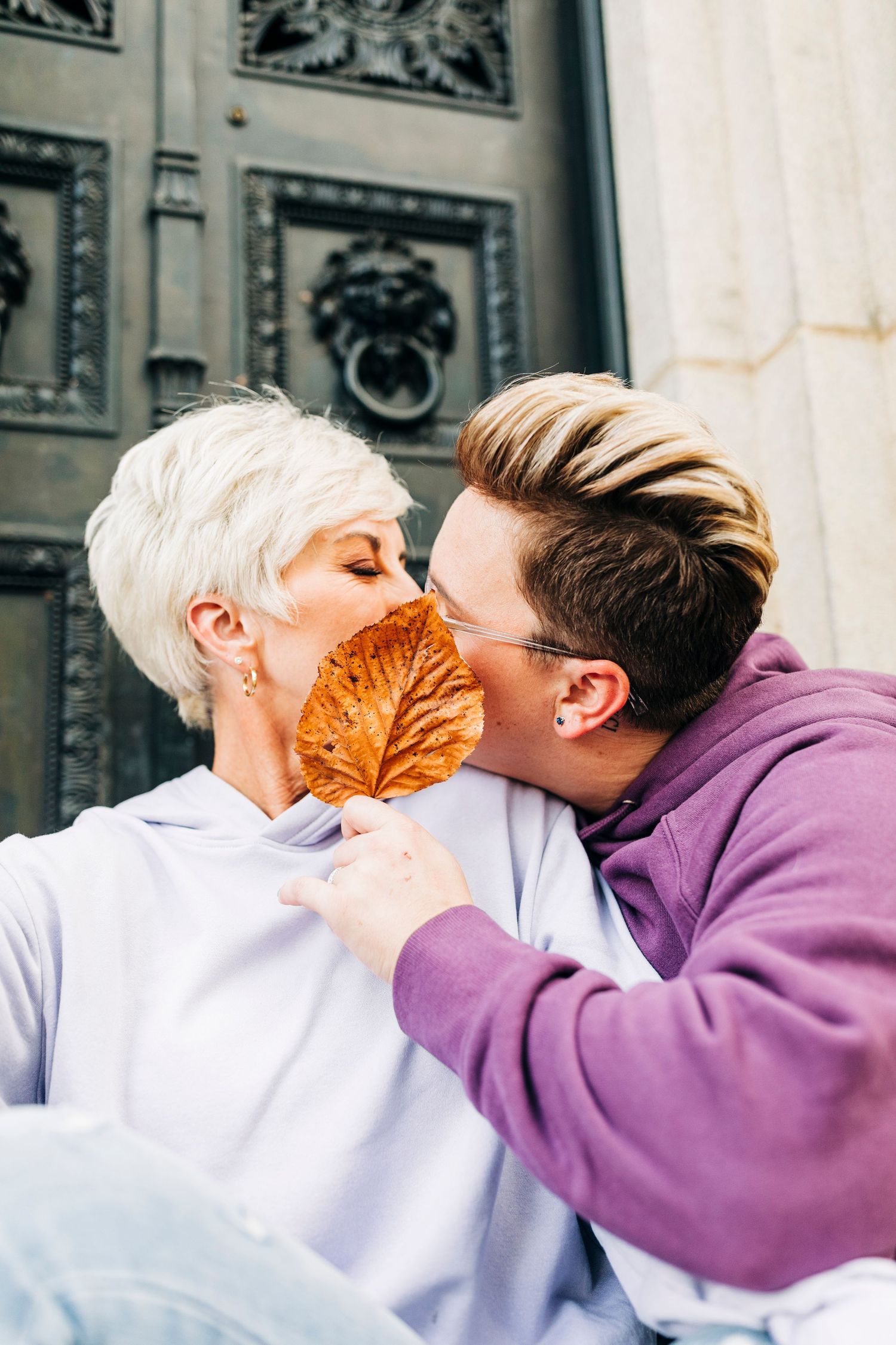 Playful couple sharing a moment with an autumn leaf between them.