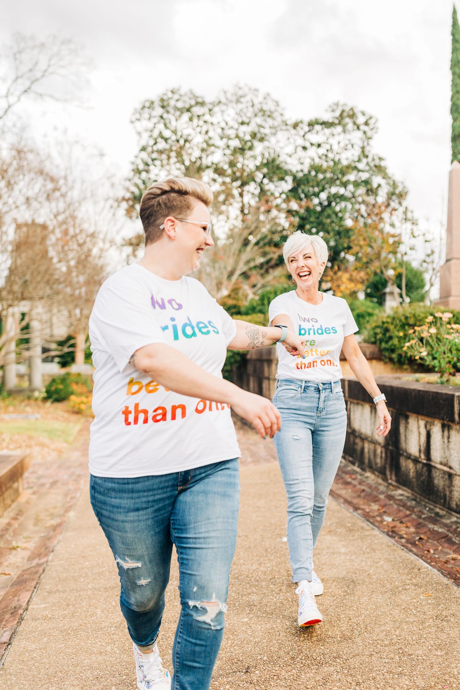Two friends laughing and walking together on a path wearing casual t-shirts and jeans on a sunny day.